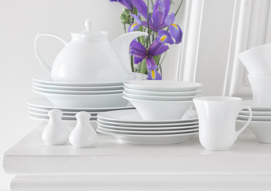 FDC White porselensservise med stablede tallerkener, skåler, kopp og tekanne i en lys borddekking med lilla blomster.