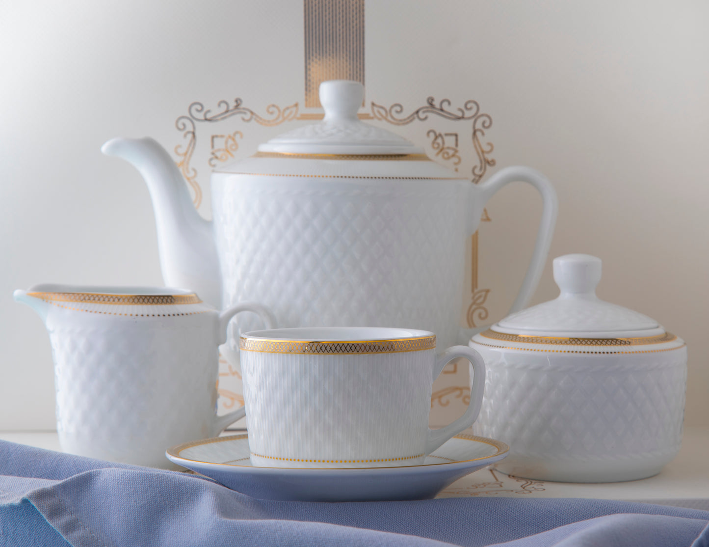 Sepinood kaffeservise i hvitt porselen med elegante gulldetaljer, med kopp og tefat i front, tekanne, sukkerskål og sausenebb.