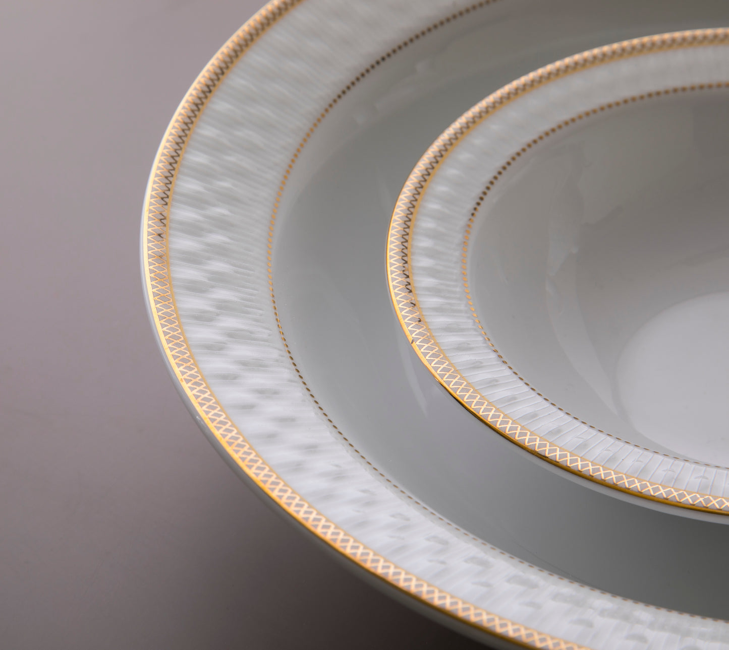 Nærbilde av Sepinood-servisets elegante gulldetaljer og strukturerte mønster langs kanten på de hvite porselenstallerkenene.