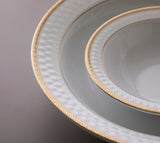 Nærbilde av Sepinood-servisets elegante gulldetaljer og strukturerte mønster langs kanten på de hvite porselenstallerkenene.