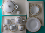 Sepinood-serviset arrangert ovenfra med suppeterrin, tallerkener, skåler, kopp, tefat og serveringsdeler i hvitt porselen med elegante gulldetaljer.