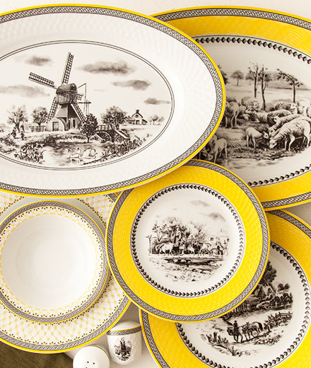 Tallerkener og serveringsfat fra Village-serviset med gule kanter og klassiske landskapsmotiver.