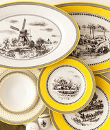 Tallerkener og serveringsfat fra Village-serviset med gule kanter og klassiske landskapsmotiver.